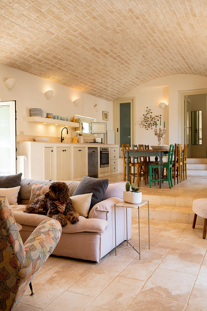 original hill house curated home redesign, countryside retreat puglia italy home with arched brick ceiling, view of living room couch and chairs with the kitchen in the background with table and colorful chairs