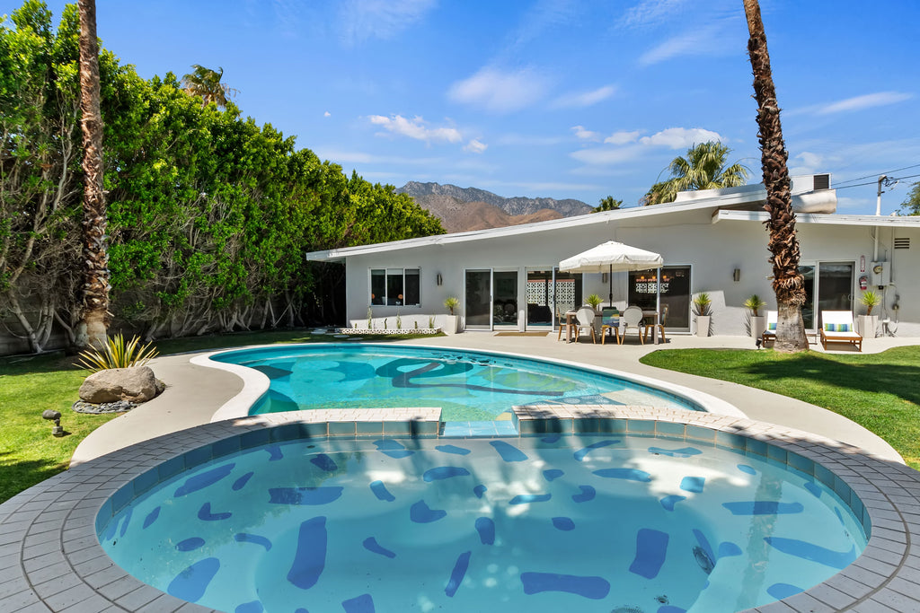 Original Curated Hill House backyard of palm springs house with alex proba hot tub, pool, grass area and outdoor seating with mountains in the background