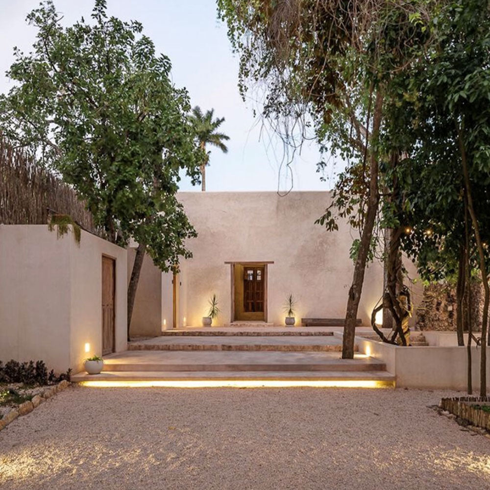 tan stucco building with vibrant stone steps and gravel with lots of trees, simplistic decor and wooden doors.