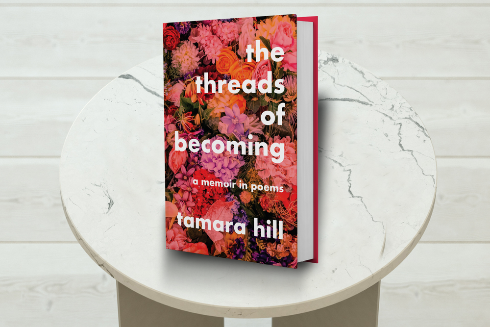 Book titled 'the threads of becoming' by Tamara Hill on a round white table with a light wooden floor background.
