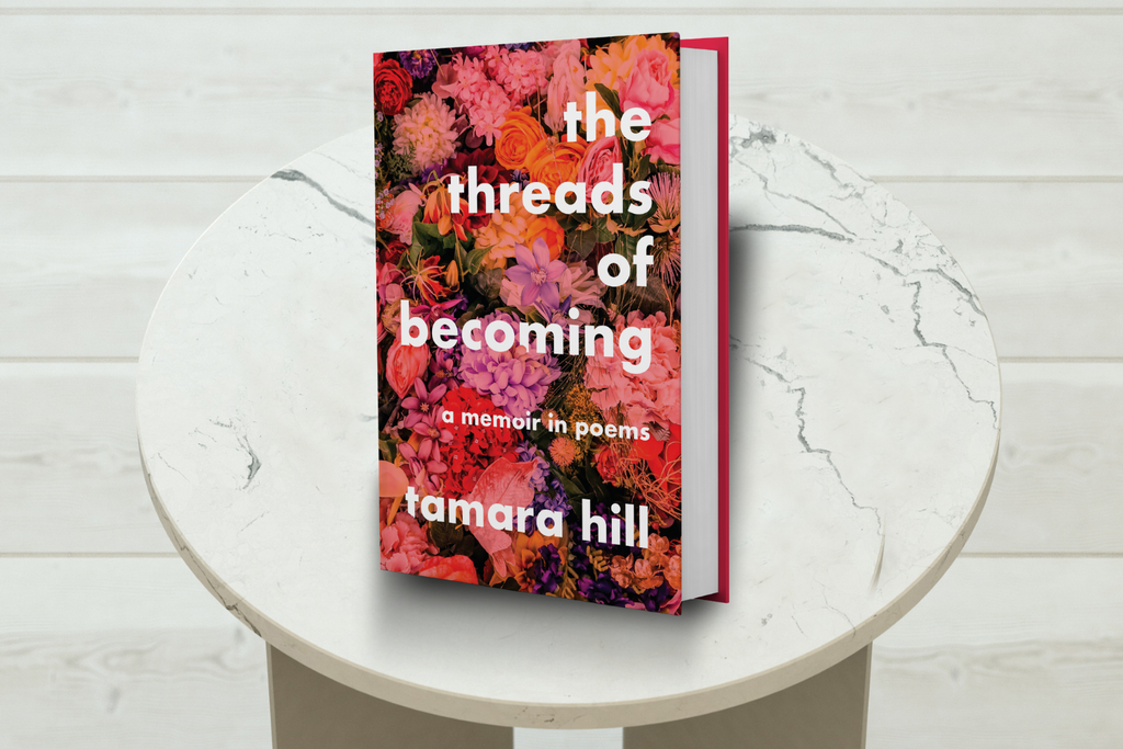 Book titled 'the threads of becoming' by Tamara Hill on a round white table with a light wooden floor background.